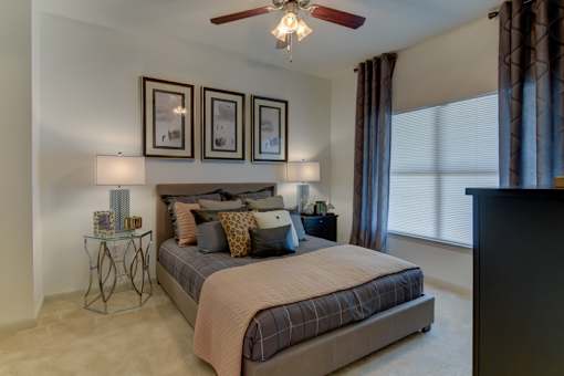 A bedroom with a bed, a ceiling fan, and a window with curtains.