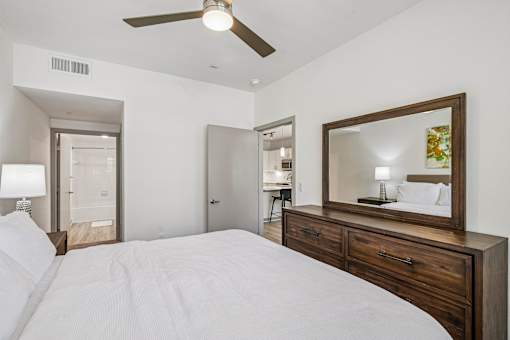 A bedroom with a large bed, a ceiling fan, and a mirror with a wooden frame.