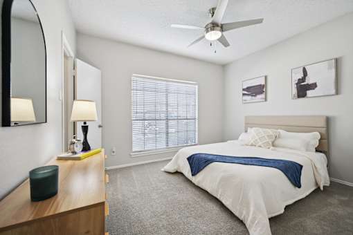 A bedroom with a bed, a dresser, a ceiling fan, and a window with blinds.