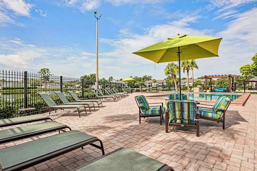 A sunny day at the poolside with green lounge chairs and a yellow umbrella.