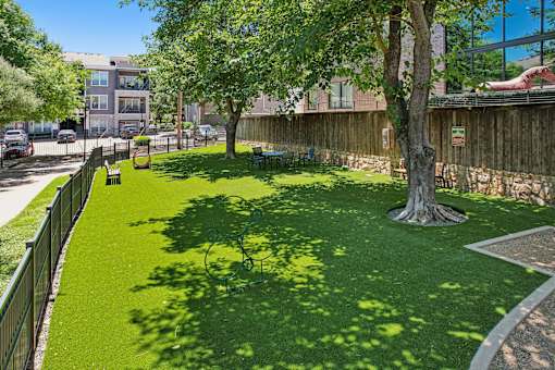 A green lawn with a tree in the middle and a fence around it.