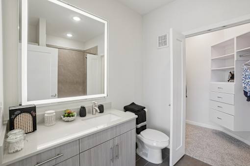 A sleek bathroom with granite countertops and backlit mirror.