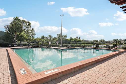 A large outdoor swimming pool with red brick edges and a clear blue sky above.