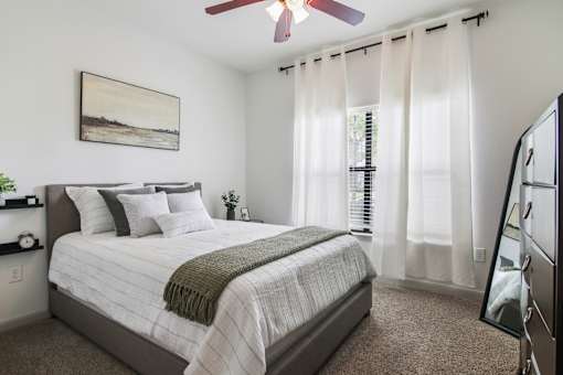 A bedroom with a bed, a ceiling fan, and a painting on the wall.