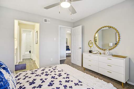 A bedroom with a bed, dresser, mirror and a ceiling fan.