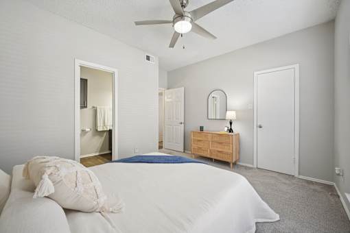 A bedroom with a bed, dresser, mirror, and a ceiling fan.