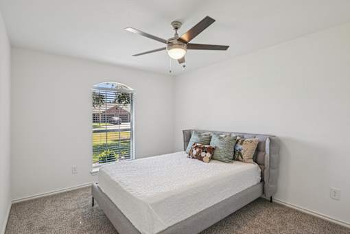 A bedroom with a bed, pillows, and a ceiling fan.