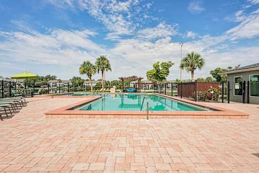 A pool surrounded by a brick patio with trees in the background.