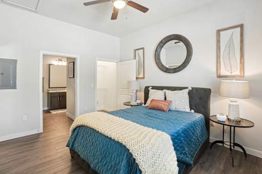 A bedroom with a bed, a mirror, a ceiling fan, and a side table.