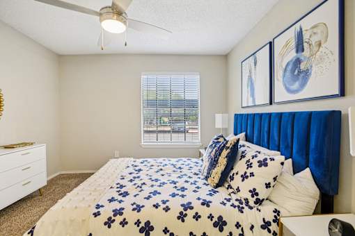 A bedroom with a bed, blue comforter, and two framed pictures on the wall.