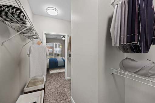 A white closet with clothes hanging and a bed in the background.