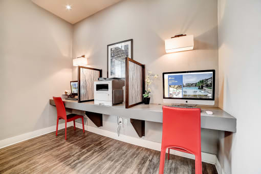 a desk with two computer monitors and two red chairs
