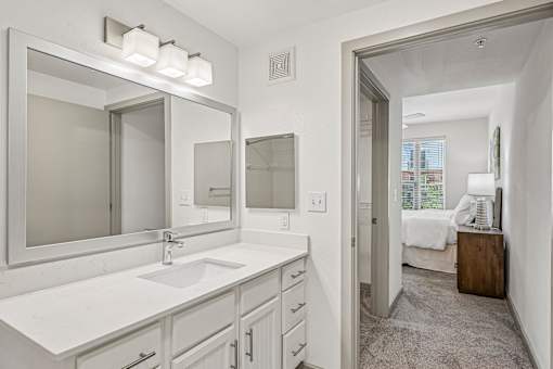 A bathroom with a sink, mirror, and a bedroom in the background.