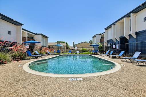 A swimming pool surrounded by lounge chairs in a residential area.