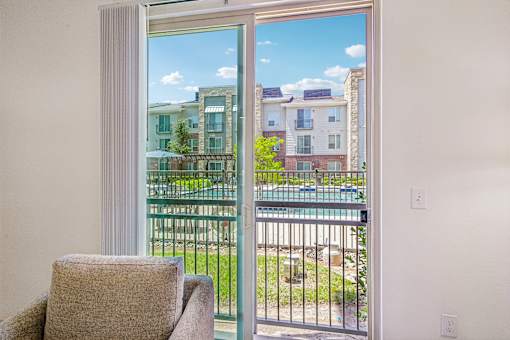 A chair sits in a room with a view of a pool and apartment buildings outside.