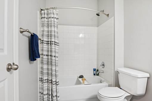 A white bathroom with a white toilet, white tub, and a white shower curtain.