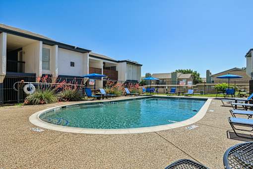 A swimming pool surrounded by lounge chairs and umbrellas in a residential area.