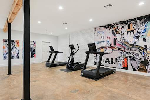 Three treadmills are lined up in a room with a colorful mural on the wall.