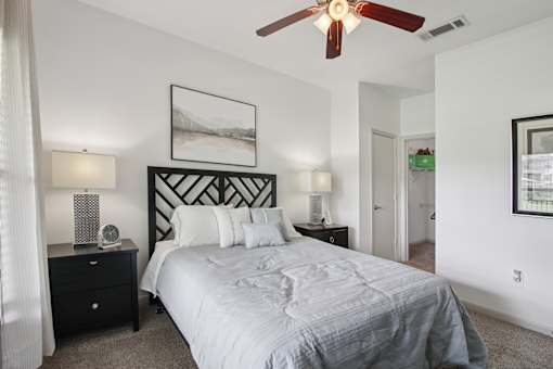 A bedroom with a large bed, a ceiling fan, and two lamps.