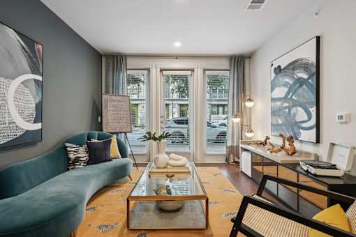 A living room with a green sofa, a coffee table, and a large window with a view of a building.
