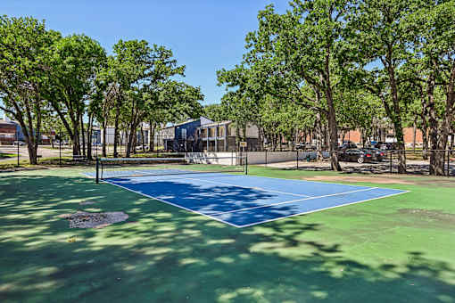 A blue and green tennis court surrounded by trees.
