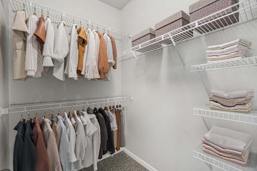 A white closet with clothes hanging and folded towels on shelves.