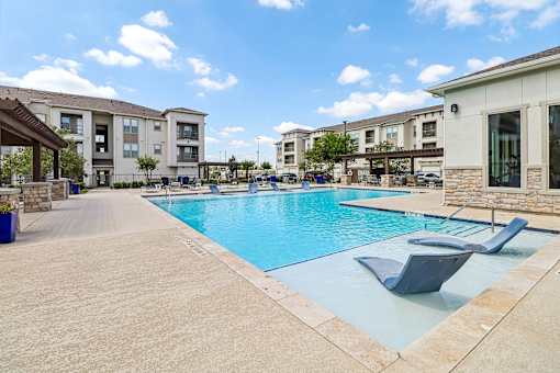 A swimming pool surrounded by lounge chairs and apartment buildings.