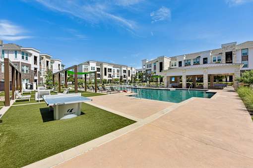 A swimming pool is surrounded by a grassy area and a concrete walkway in a residential area.