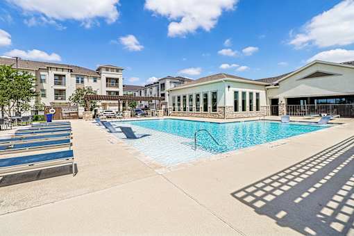 A swimming pool surrounded by a concrete patio and a building in the background.