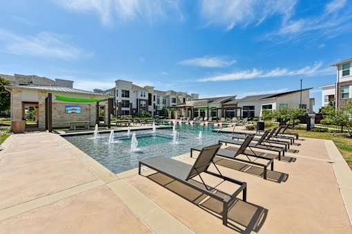 A pool with a fountain and lounge chairs in front of apartment buildings.