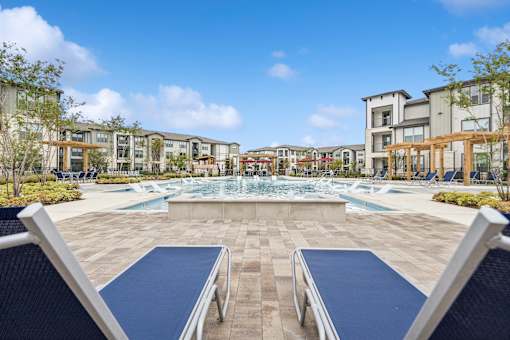 A swimming pool surrounded by a stone patio and lounge chairs.