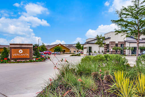Landscaped entry feature beside driveway with community buildings in the background.