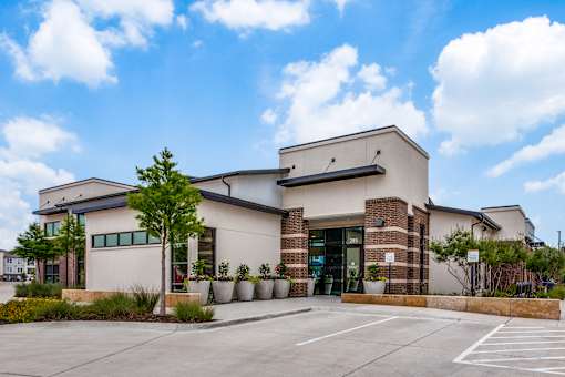 Modern community building exterior with brick accents, planters, and landscaped beds.