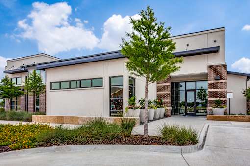 Front entrance with glass doors, shade tree, and decorative planters in Burleson, TX.
