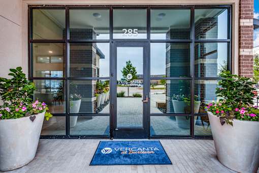 Glass-front building entry with covered walkway and planters at Vercanta at Burleson.
