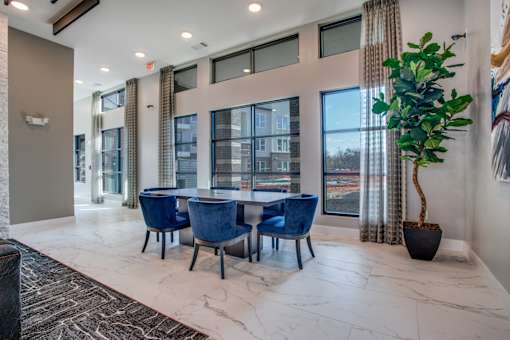 Clubroom table seating beside oversized windows and high ceilings.
