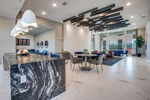 Clubhouse social space with stone-topped island, pendant lighting, and seating areas.