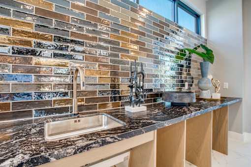 Wet bar counter with sink, stone surface, and shimmering tile backsplash.
