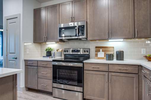 Stainless range and microwave framed by wood cabinetry and tile backsplash.