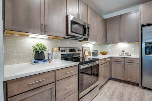 L-shaped apartment kitchen with white countertops, under-cabinet lighting, and modern cabinetry.