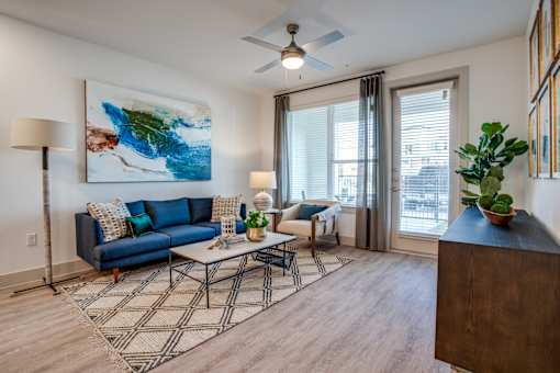 Spacious living room with blue sofa, ceiling fan, and balcony door with blinds.