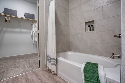 Soaking tub with tiled surround and built-in niche beside walk-in closet.