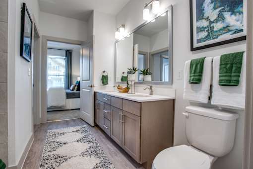 Extended bathroom vanity with bright lighting and view toward bedroom doorway.