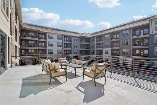 A patio with chairs and a table is in front of apartment buildings.