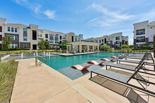 A pool with sun loungers in front of apartment buildings.