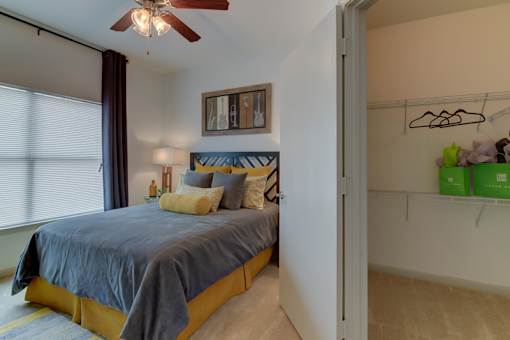 A bedroom with a bed, pillows, a ceiling fan, and a window with curtains.