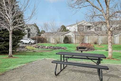 A black picnic table is in the foreground of a grassy area with a house in the background.
