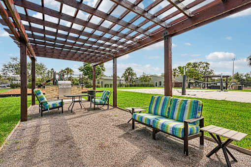 A wooden pergola with a striped couch and two chairs.