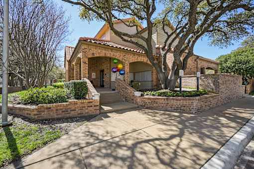 A house with a brick wall and a tree in front.