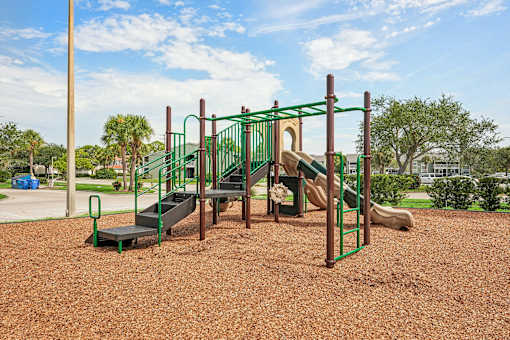 A playground with a green slide and a brown sandy ground.